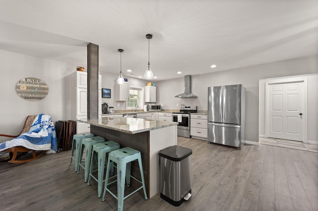 kitchen with white cabinets, wall chimney exhaust hood, dark wood-type flooring, appliances with stainless steel finishes, and a center island