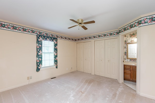 unfurnished bedroom featuring two closets, ceiling fan, light colored carpet, and ensuite bathroom