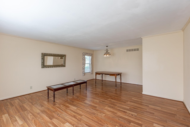 unfurnished room with an inviting chandelier, light wood-type flooring, and crown molding