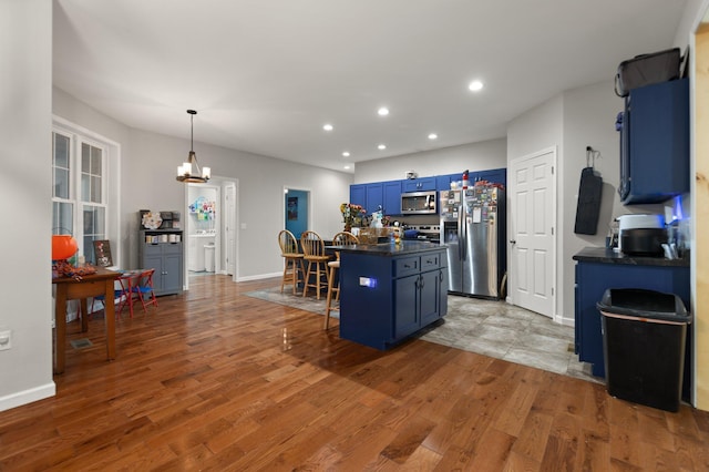 kitchen featuring appliances with stainless steel finishes, a breakfast bar, blue cabinetry, wood-type flooring, and a center island