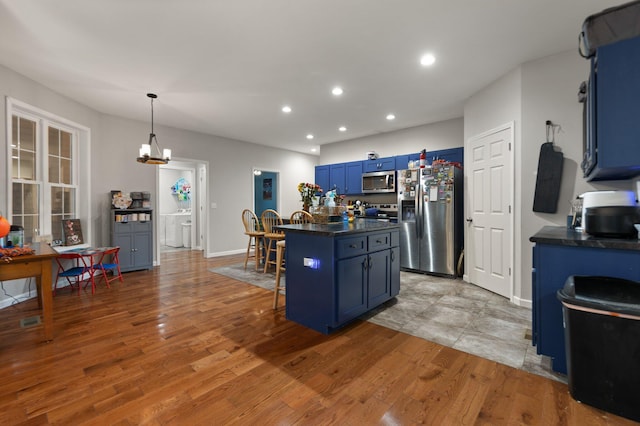 kitchen with blue cabinetry, a center island, stainless steel appliances, pendant lighting, and a kitchen bar