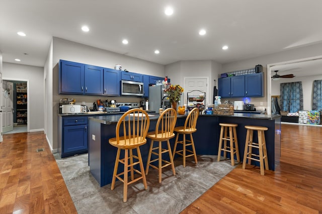 kitchen featuring ceiling fan, a kitchen bar, blue cabinets, and appliances with stainless steel finishes