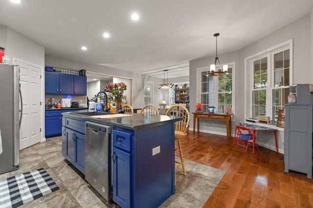 kitchen with a breakfast bar, blue cabinetry, stainless steel appliances, and a kitchen island with sink