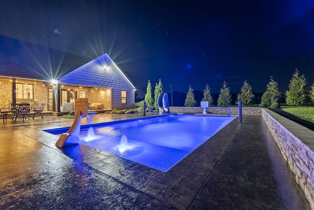 pool at twilight with a patio and a water slide