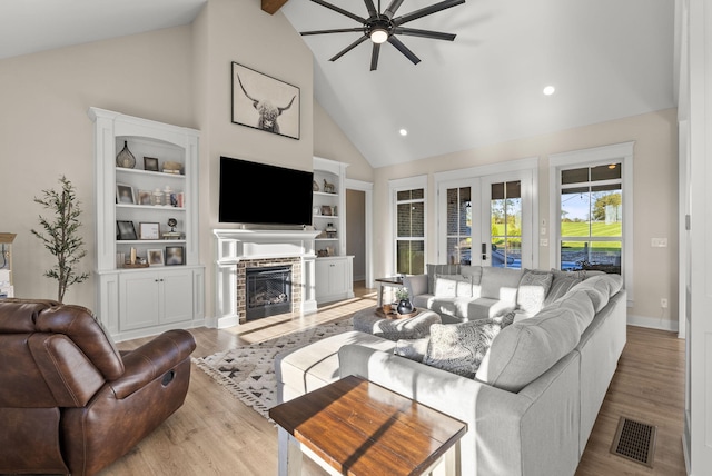 living room with ceiling fan, high vaulted ceiling, a fireplace, light hardwood / wood-style floors, and french doors