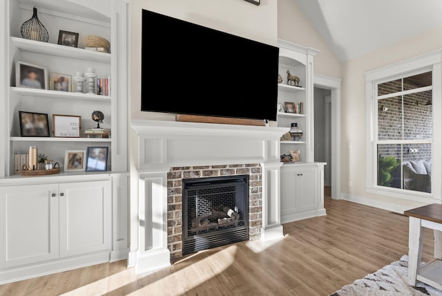 living room featuring light hardwood / wood-style flooring, built in shelves, vaulted ceiling, and a brick fireplace