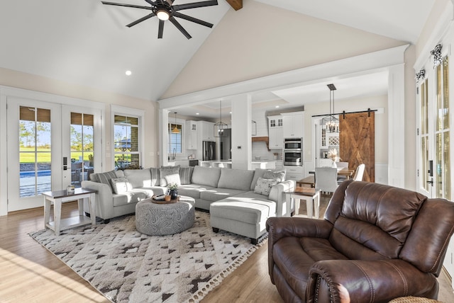 living room with beam ceiling, hardwood / wood-style floors, a barn door, high vaulted ceiling, and ceiling fan