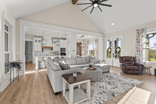 living room featuring beam ceiling, high vaulted ceiling, light hardwood / wood-style flooring, and ceiling fan with notable chandelier