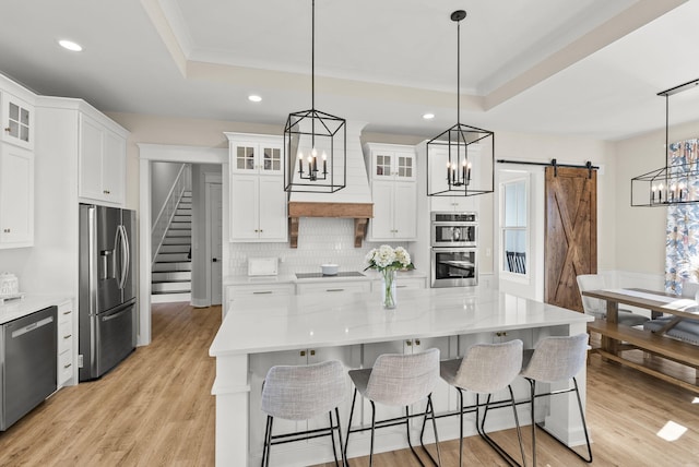 kitchen with stainless steel appliances, hanging light fixtures, a barn door, and white cabinets