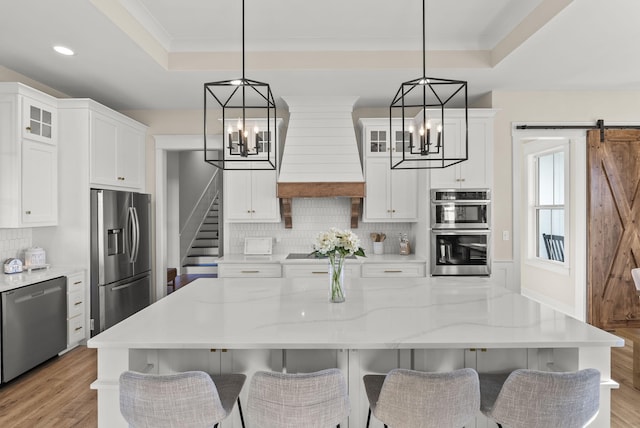 kitchen with stainless steel appliances, a barn door, decorative light fixtures, custom exhaust hood, and white cabinetry