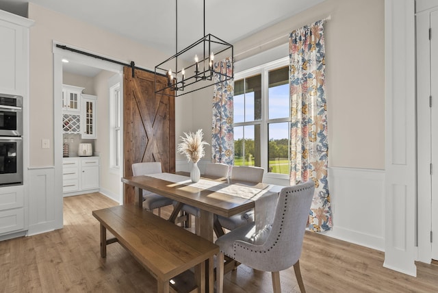 dining area with a barn door, a notable chandelier, and light wood-type flooring