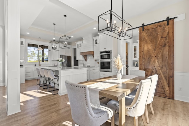 dining area featuring light hardwood / wood-style floors, ornamental molding, a barn door, and a tray ceiling