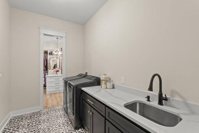 laundry area with cabinets, light tile patterned floors, an inviting chandelier, washer and dryer, and sink