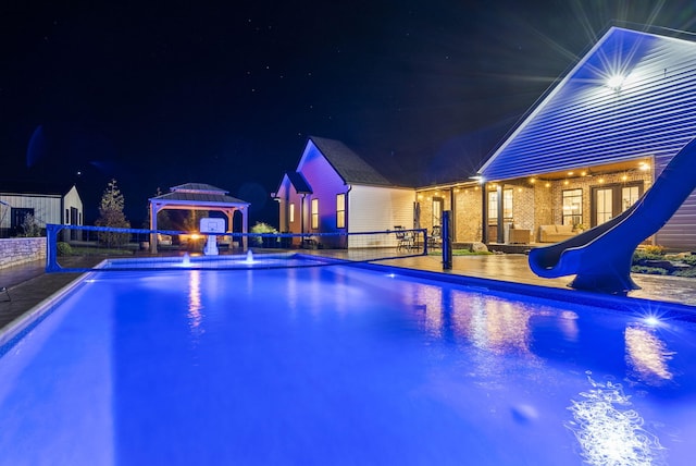 pool at night featuring a gazebo, a water slide, and a patio area