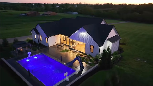 pool at dusk with a patio, a water slide, and a yard