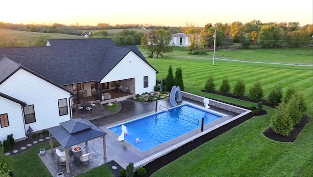 pool at dusk featuring a patio, a water slide, and a lawn