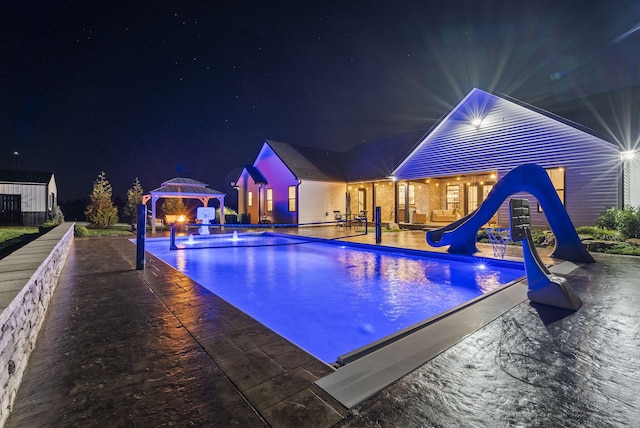 pool at night featuring a gazebo, a water slide, and a patio area