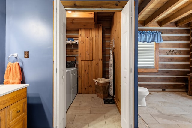 bathroom with vanity, wood walls, toilet, and washing machine and clothes dryer