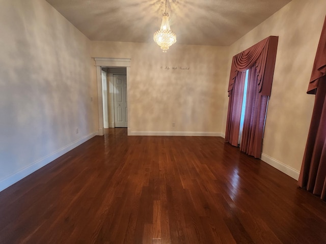 empty room featuring a notable chandelier and dark hardwood / wood-style floors