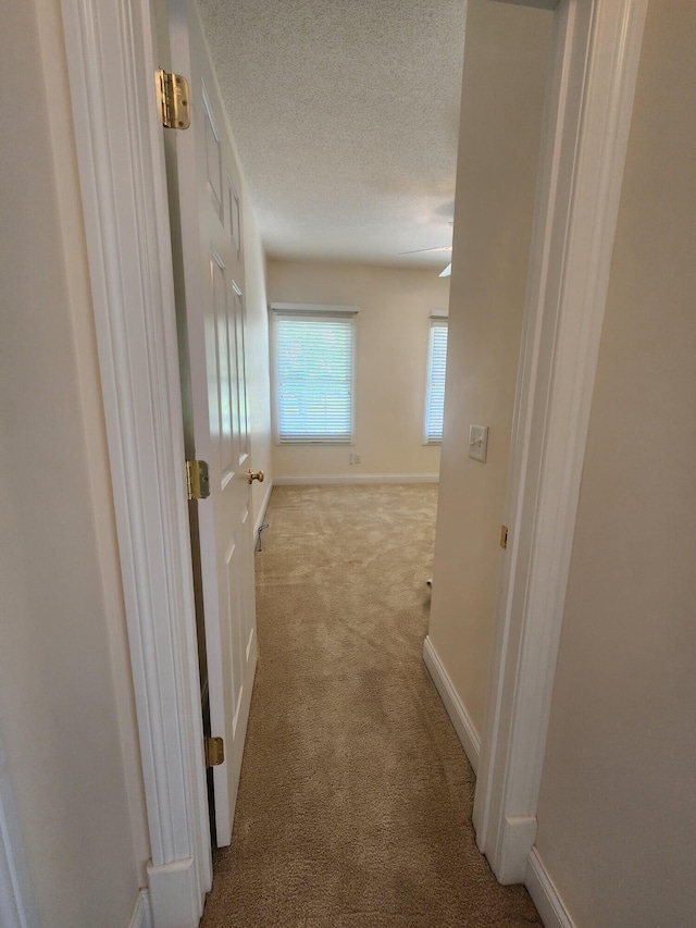 hallway featuring a textured ceiling and light colored carpet