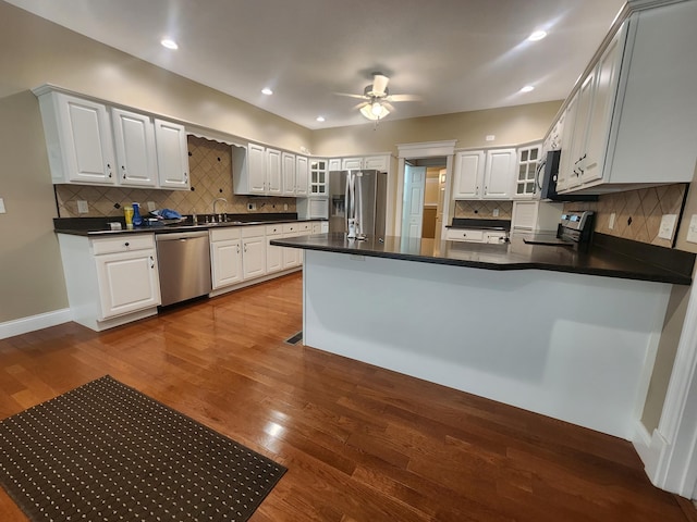 kitchen with hardwood / wood-style flooring, white cabinetry, kitchen peninsula, backsplash, and appliances with stainless steel finishes