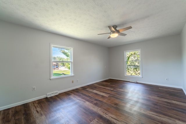 empty room featuring dark wood-type flooring, visible vents, and a healthy amount of sunlight