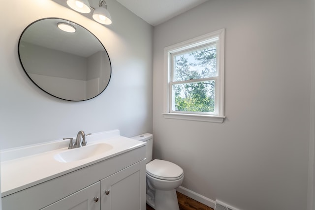 half bath featuring baseboards, vanity, and toilet