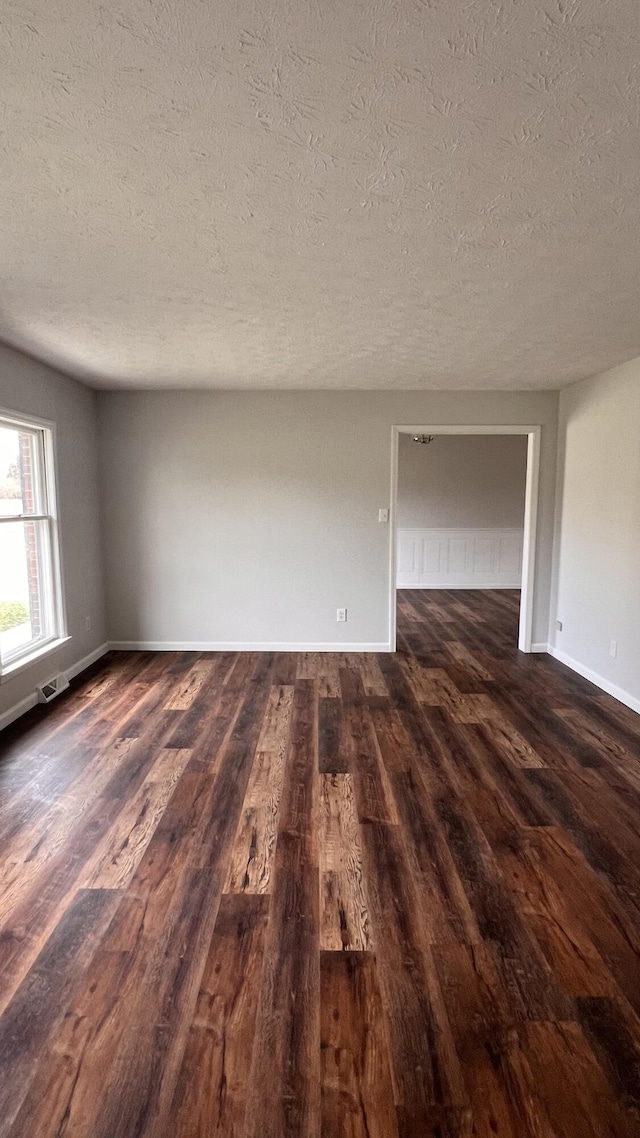 empty room with baseboards, visible vents, and dark wood finished floors