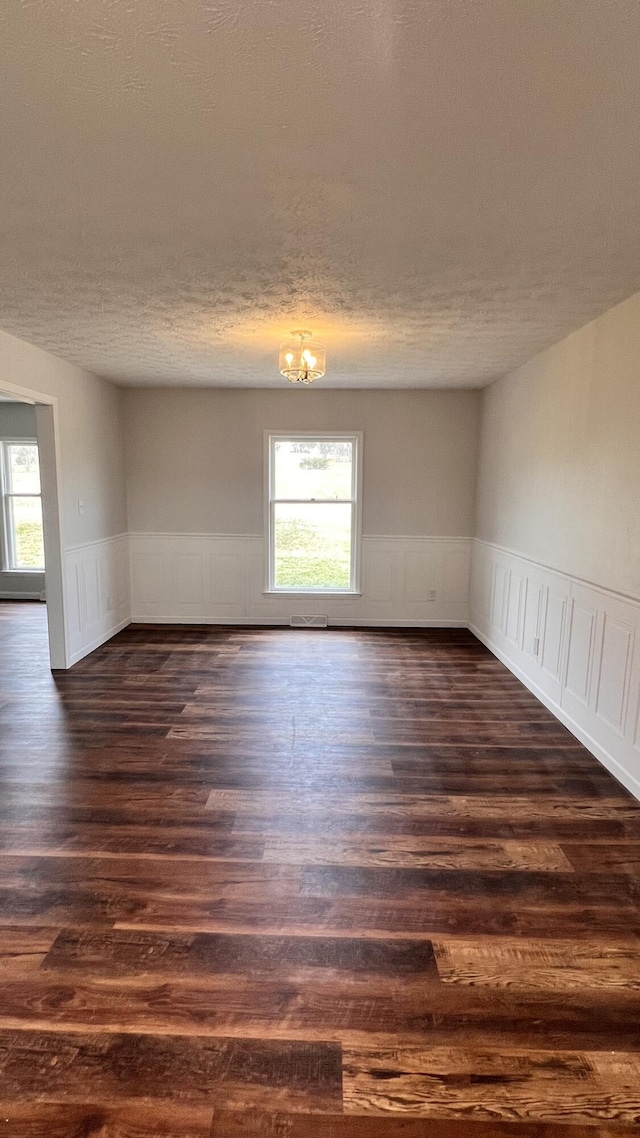 unfurnished room featuring dark wood-style floors, a textured ceiling, and wainscoting