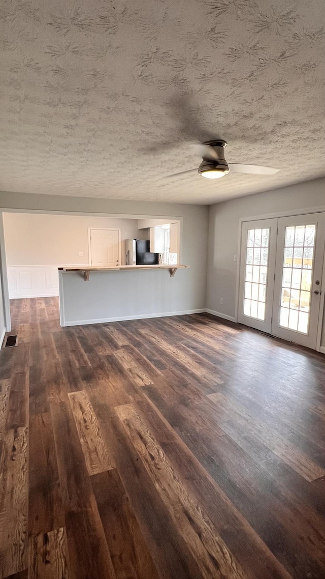 unfurnished living room with baseboards, visible vents, a ceiling fan, dark wood-style flooring, and a textured ceiling