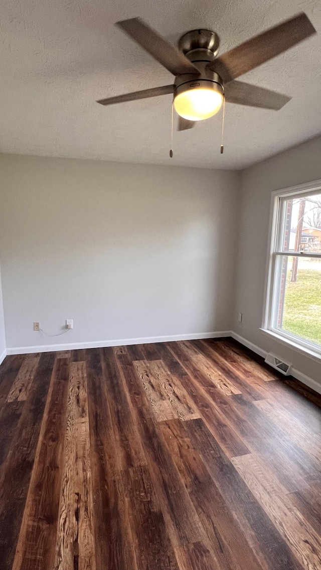 spare room with a textured ceiling, a ceiling fan, visible vents, baseboards, and dark wood-style floors