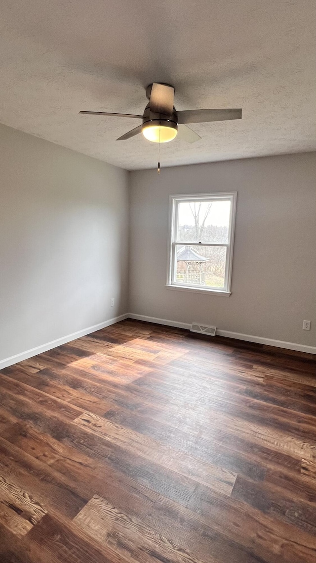 unfurnished room featuring dark wood-style flooring, visible vents, a textured ceiling, and baseboards