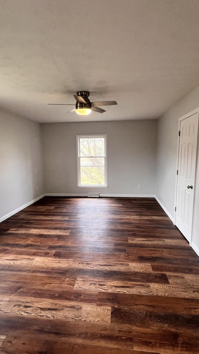 empty room with a textured ceiling, dark wood finished floors, a ceiling fan, and baseboards