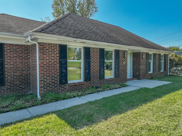 exterior space with brick siding, roof with shingles, and a front yard