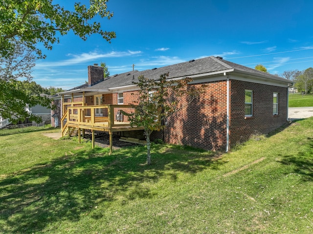 back of property featuring a wooden deck, a chimney, a lawn, and brick siding