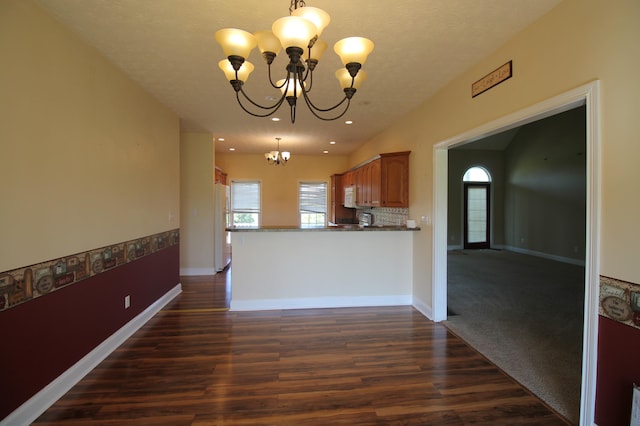 kitchen with dark wood-type flooring, kitchen peninsula, an inviting chandelier, white appliances, and decorative light fixtures