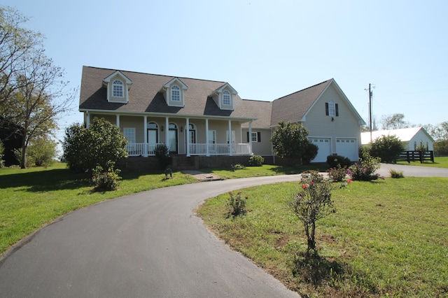 new england style home featuring covered porch, a front yard, and a garage