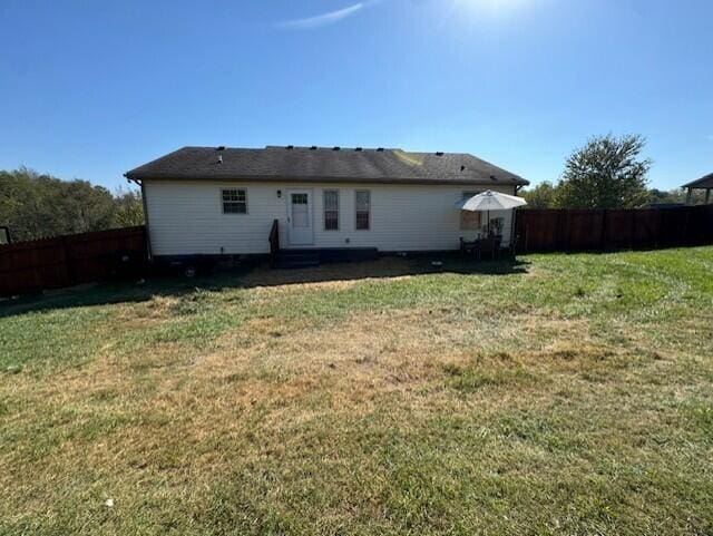 rear view of property featuring a fenced backyard and a yard