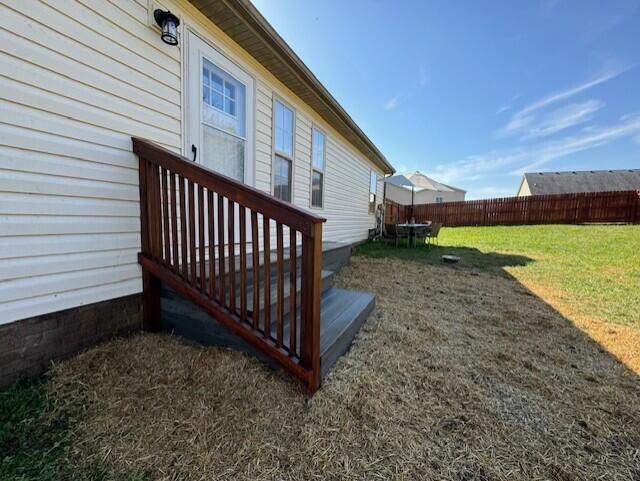 view of side of home featuring fence, a wooden deck, and a lawn