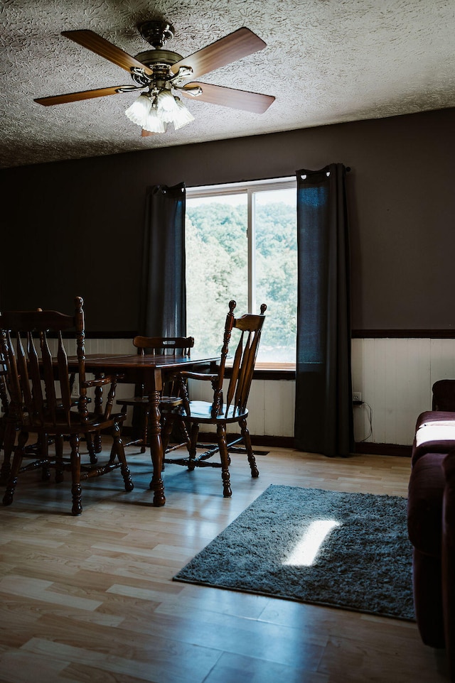 dining space featuring light wood-type flooring, a textured ceiling, wooden walls, and ceiling fan