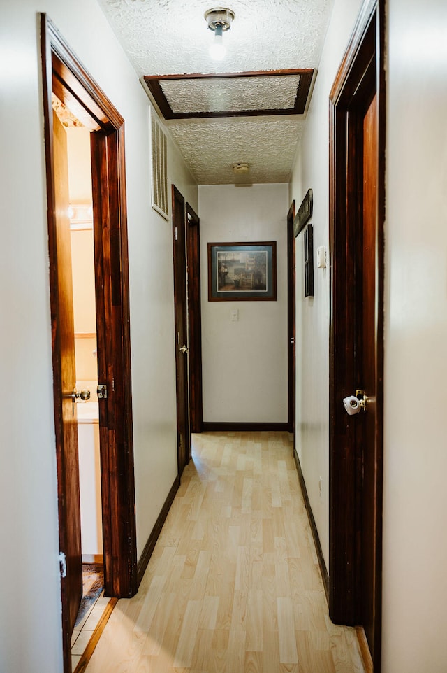 corridor featuring a textured ceiling and light hardwood / wood-style flooring