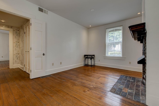 unfurnished room featuring wood-type flooring and a tiled fireplace