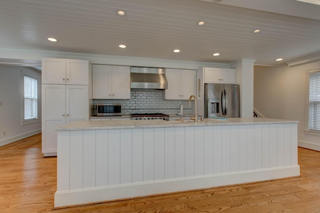 kitchen with appliances with stainless steel finishes, white cabinetry, a kitchen island with sink, and wall chimney range hood