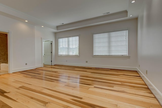 empty room with light hardwood / wood-style floors, a raised ceiling, and ornamental molding