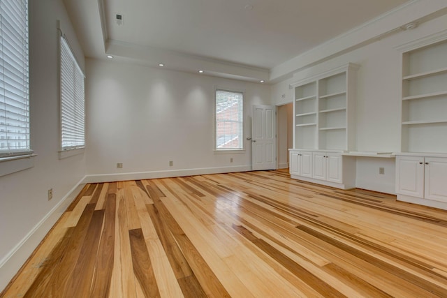 interior space featuring built in features, light wood-type flooring, a raised ceiling, and built in desk