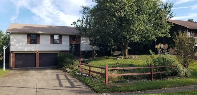 bi-level home featuring an attached garage, fence, a front yard, and concrete driveway