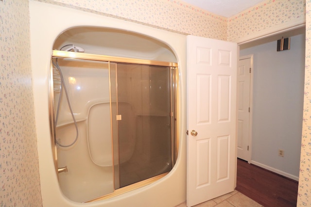 bathroom with bath / shower combo with glass door and wood-type flooring