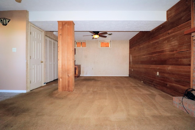 unfurnished living room featuring ceiling fan, wooden walls, and carpet flooring