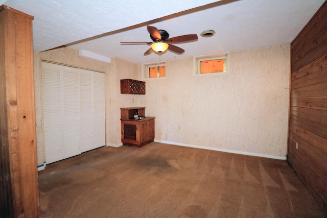 unfurnished bedroom with dark carpet, wooden walls, a closet, and ceiling fan