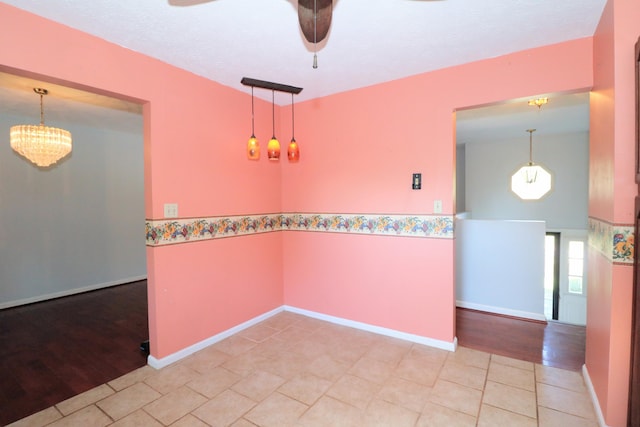 empty room featuring baseboards, ceiling fan with notable chandelier, and light tile patterned flooring